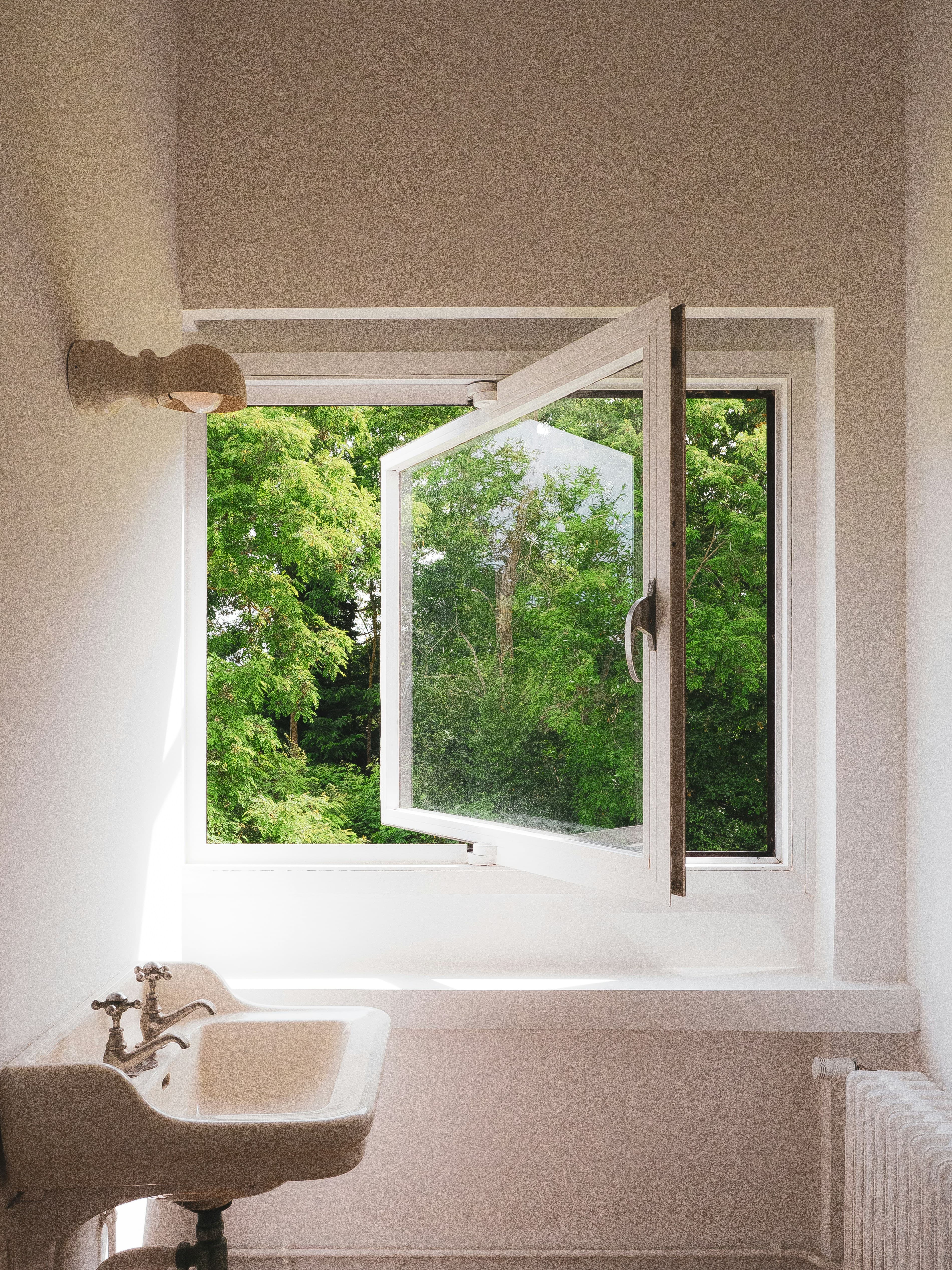 Geöffnetes weißes Fenster mit Blick auf grüne Bäume in einem hellen Bad