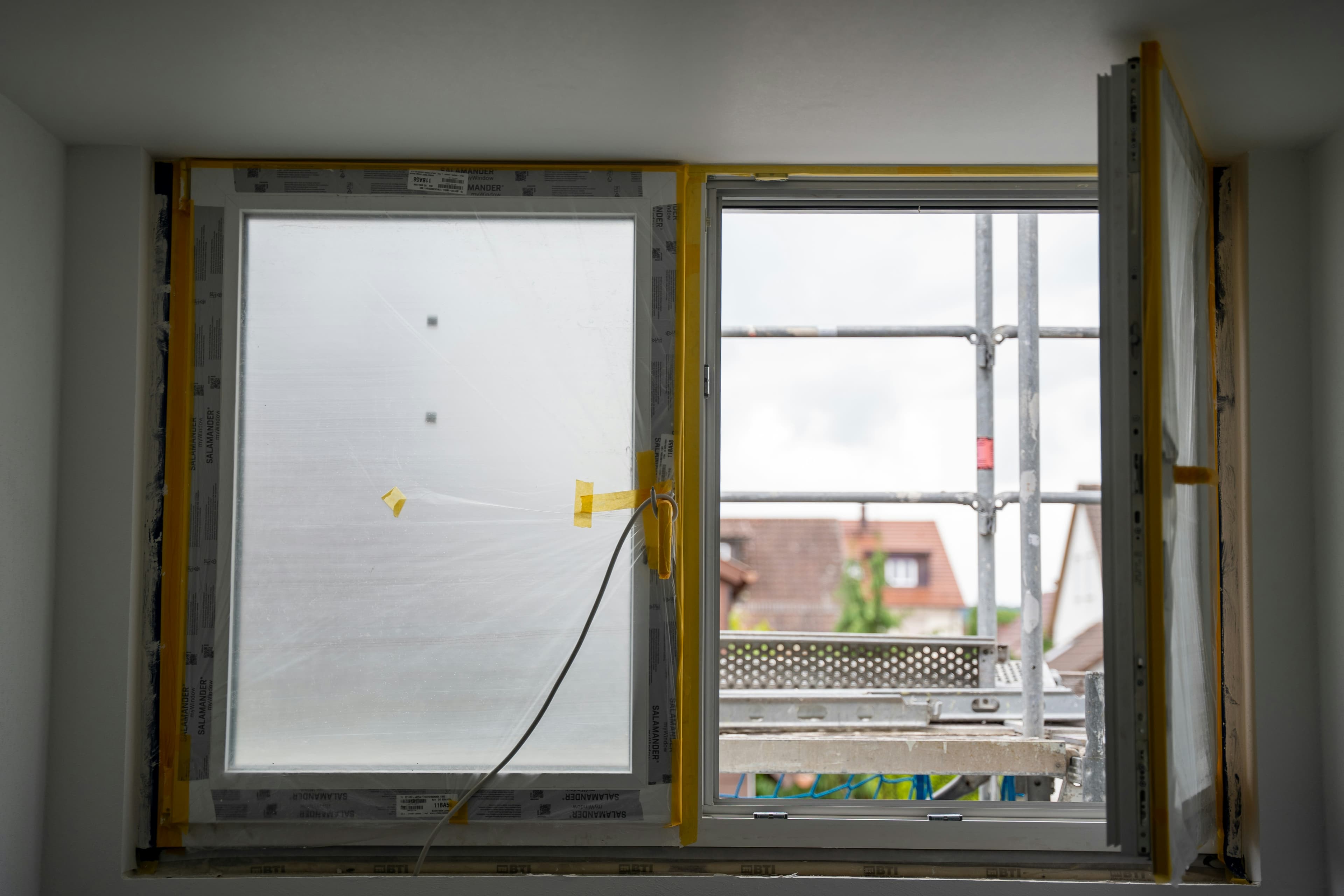 Neu eingebautes Fenster mit Schutzfolie und Anschlussband, Gerüst vor dem Haus