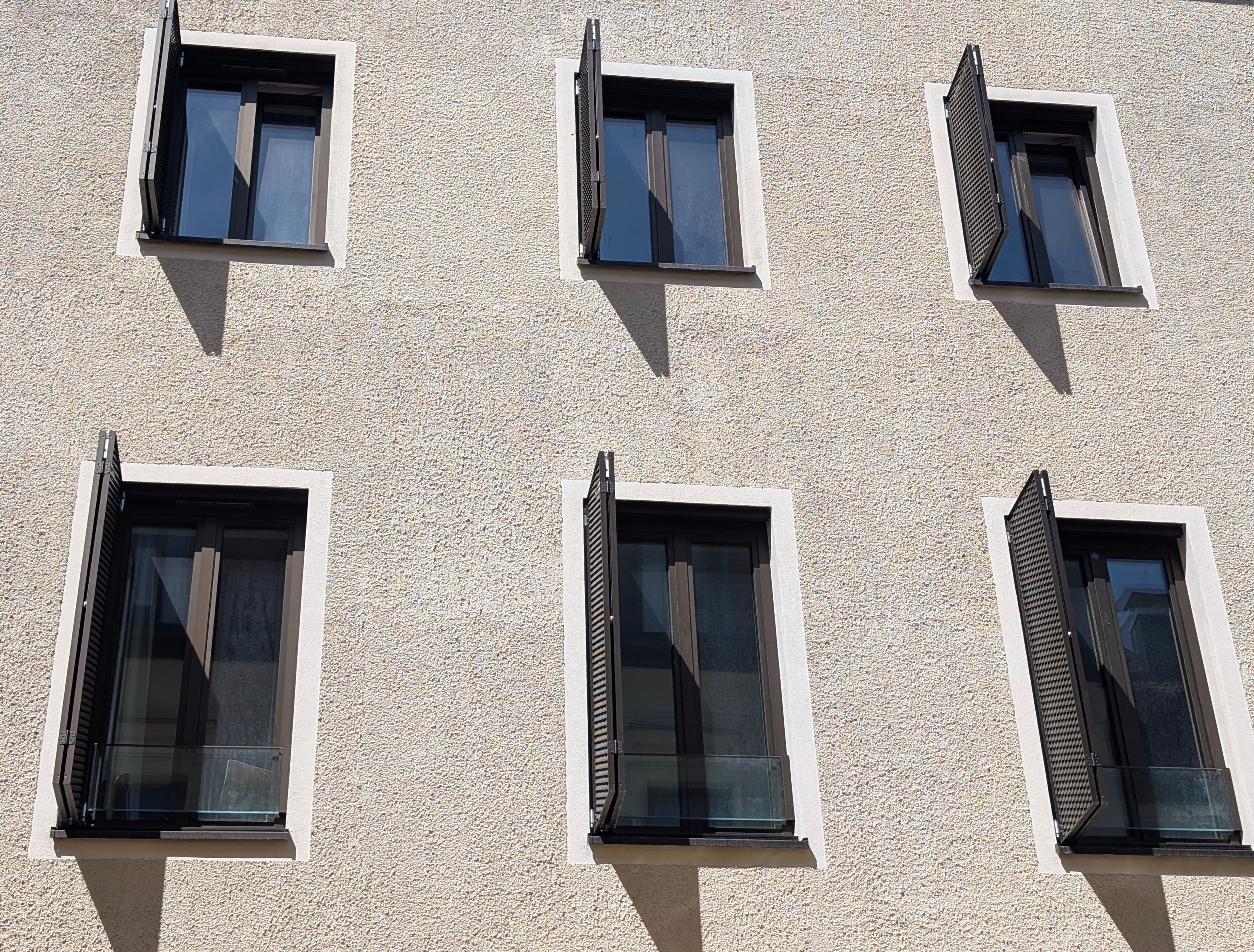 Moderne Fassade mit mehreren dunklen Aluminiumfenstern und geöffneten Fensterläden