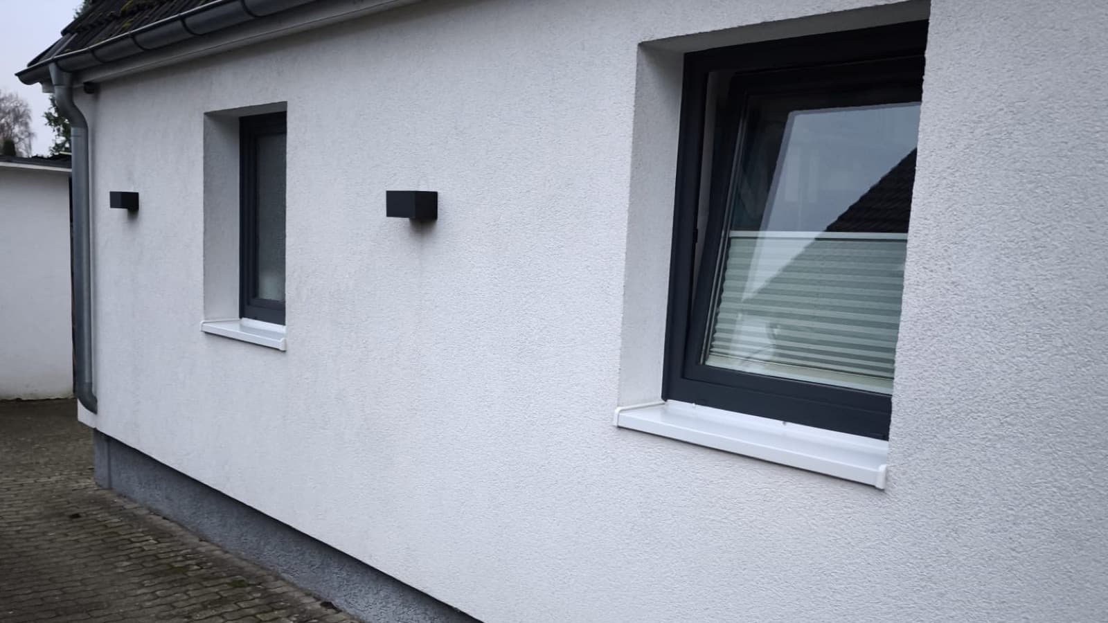 Hausfassade mit neu eingebauten anthrazitfarbenen Fenstern und weißen Fensterbänken