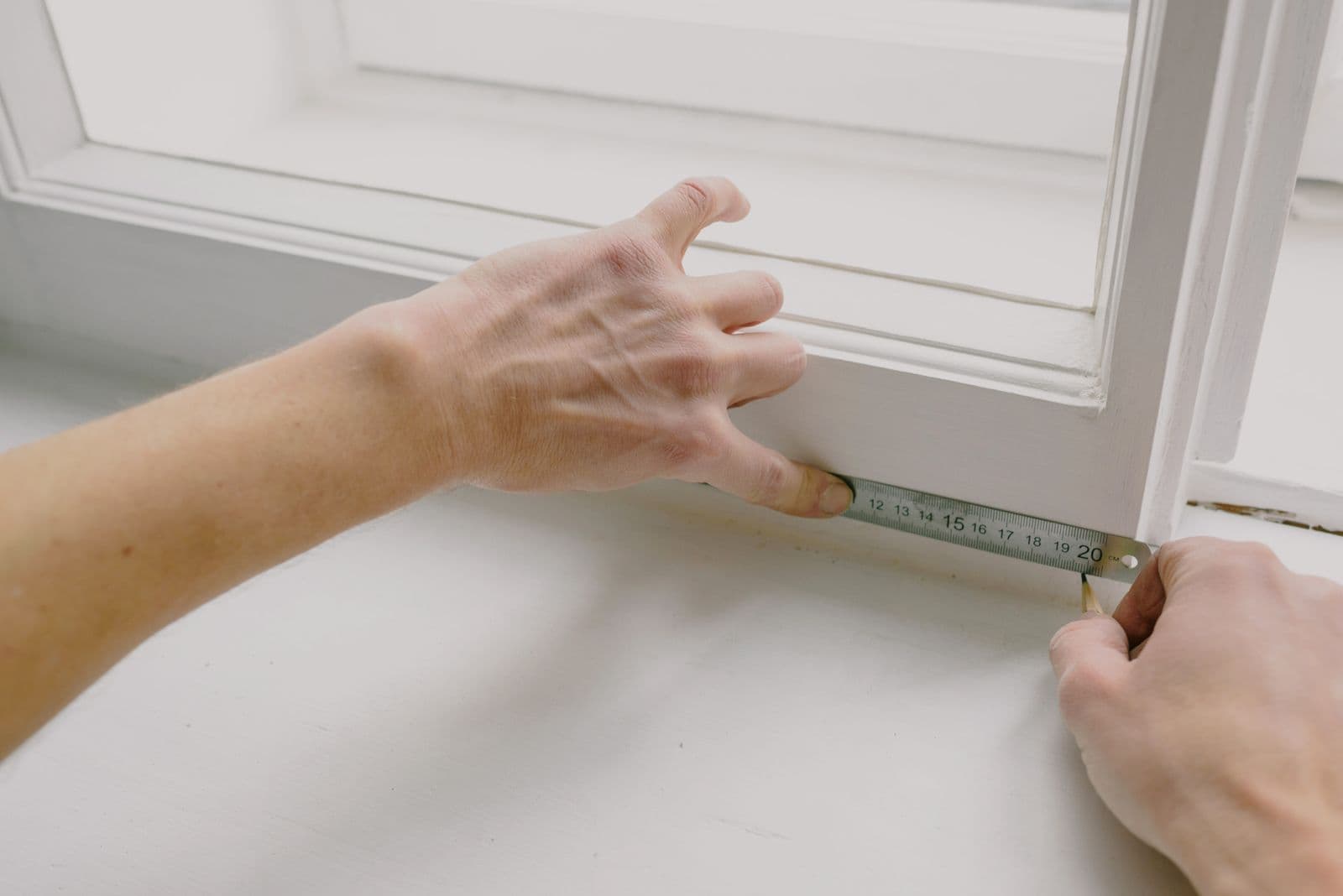 Hände nehmen Maß an einem weißen Fensterrahmen